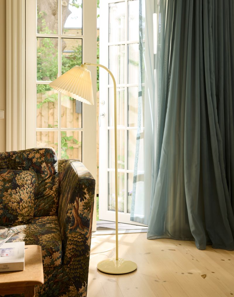Medina Gulvlampe Cream placeret ved siden af sofaen for dens behagelige belysning